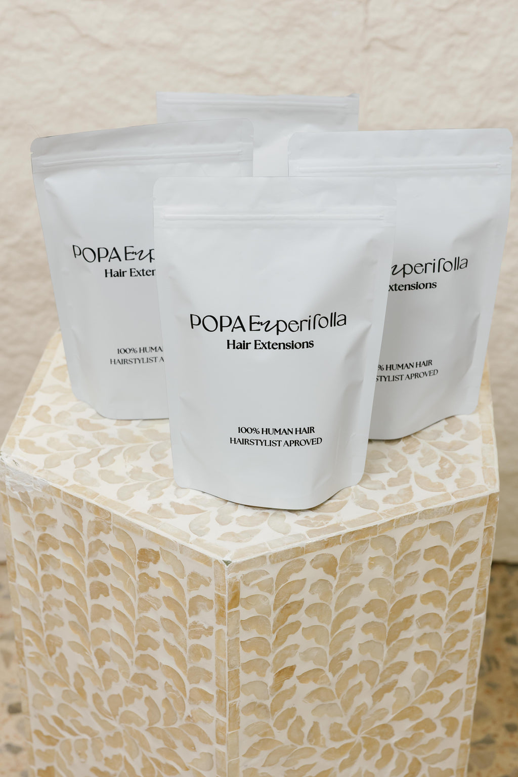Empaques de extensiones de cabello 100% humano Popa Emperifolla sobre pedestal decorativo - Popa Emperifolla Beauty Studio