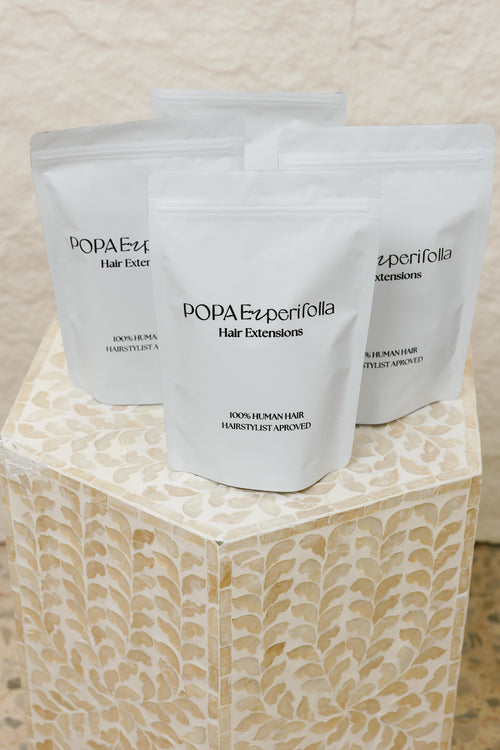Empaques de extensiones de cabello 100% humano Popa Emperifolla sobre pedestal decorativo - Popa Emperifolla Beauty Studio